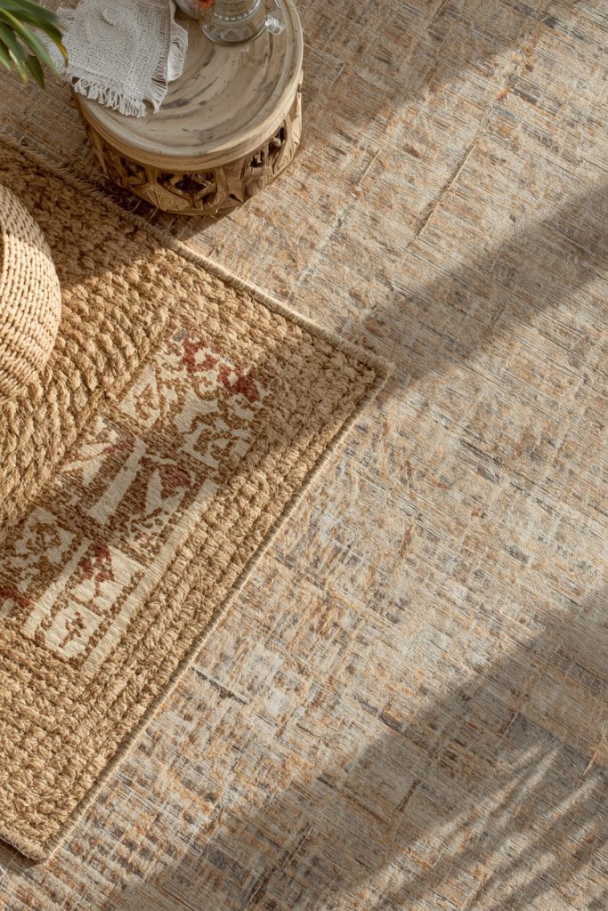 Layered rugs with jute base and vintage rug on top in warm natural light overhead view