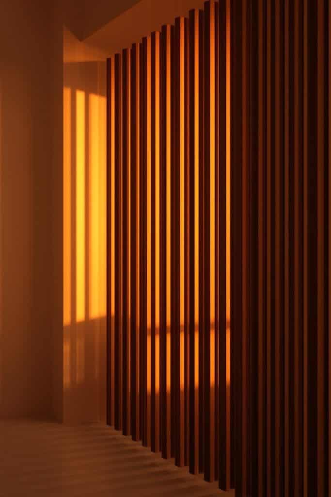 Wooden slatted screen casting warm lamp shadows on wall in a cozy golden studio interior