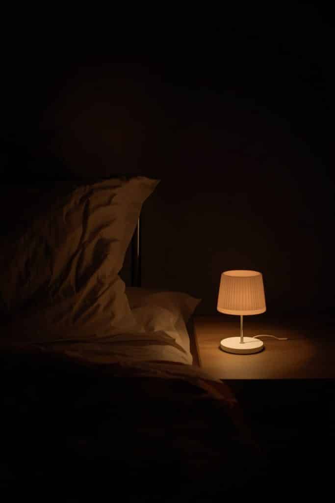 Warm bedside lamp lighting a white pillow in a dark cozy bedroom setting